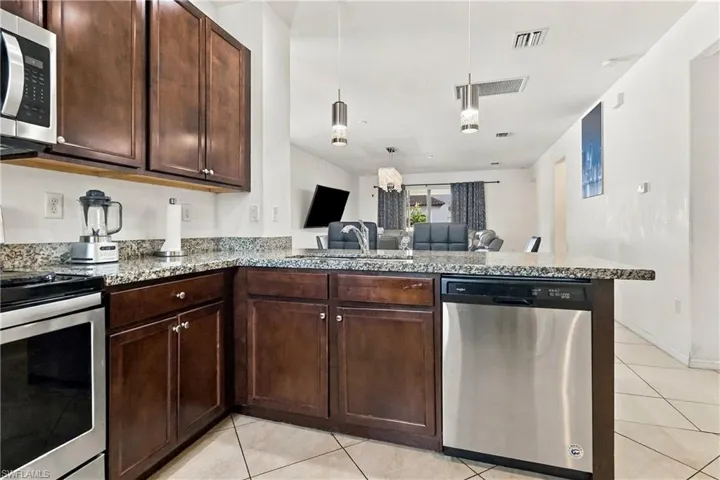 Kitchen featuring wood-finish cabinetry, granite countertops, stainless steel appliances, and tile flooring