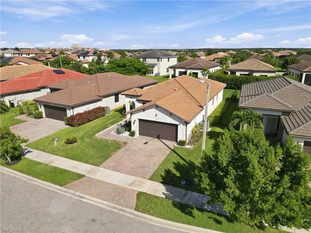 Paved driveway with an integrated walkway, mature landscaping, and a tile roof