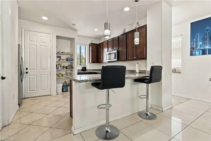Kitchen featuring dark wood-finish cabinetry, granite-style countertops, stainless steel appliances, and pendant lighting