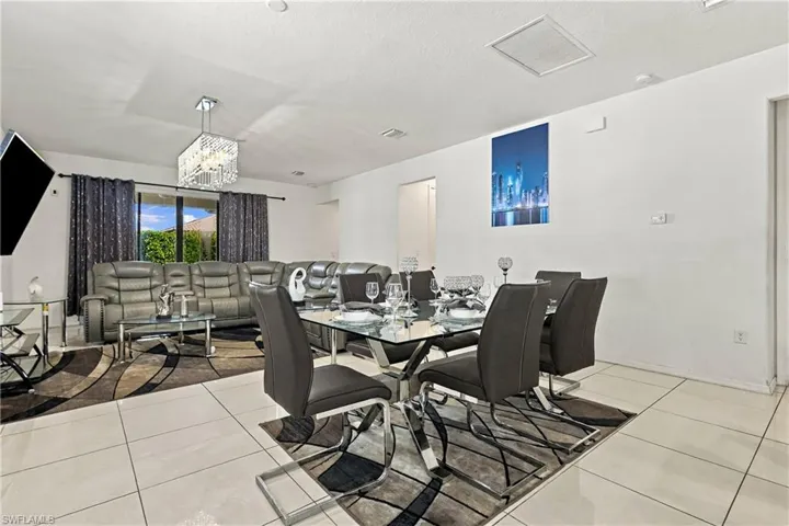 Open-concept living space with large format tile flooring, a glass-top dining table, and a contemporary chandelier