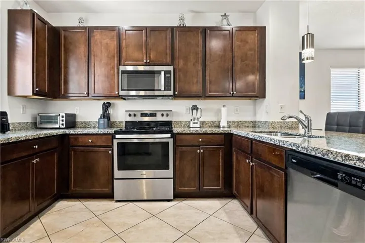 U-shaped kitchen with wood-finish cabinetry, stainless steel appliances, speckled stone countertops, and diagonal tile flooring