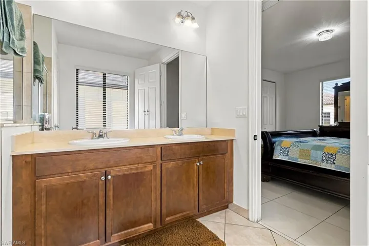 Dual basin vanity with wood-finish cabinetry, tile flooring, and a large wall-mounted mirror