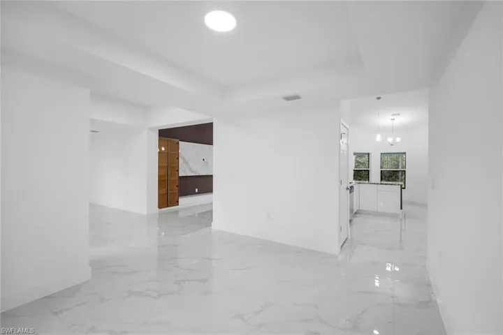 Empty room with a chandelier, a raised ceiling, and light marble finish flooring