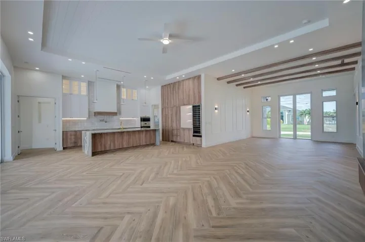 Two tone kitchen with open floor plan, a large island with sink, two tone cabinetry, ceiling fan, and modern cabinets