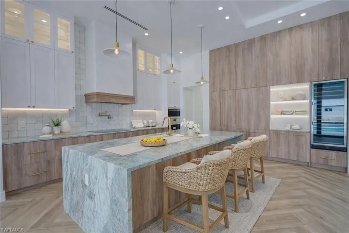Two tone kitchen with light stone counters, a kitchen bar, parquet flooring, glass insert cabinets, and two tone cabinets