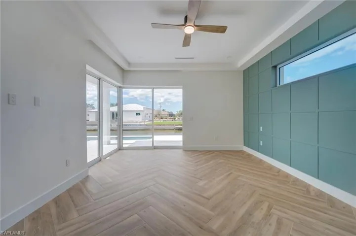 Empty room with healthy amount of natural light, ceiling fan, parquet flooring, and an accent wall