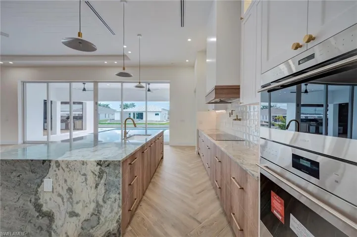 Dual tone kitchen featuring light stone counters, stainless steel double oven, parquet flooring, a large island, and dual tone cabinets