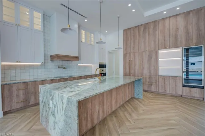 Two tone kitchen with light stone counters, beverage cooler, parquet floors, two tone cabinetry, and glass fronted cabinets