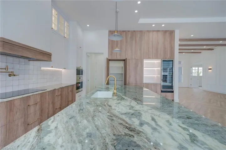 Kitchen featuring two tone color scheme, light stone counters, glass insert cabinets, modern cabinets, and black electric stovetop