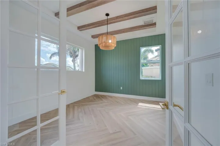 Unfurnished dining area featuring parquet flooring, wooden walls, beam ceiling, and french doors