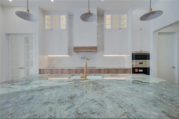 Dual tone kitchen with glass fronted cabinets, decorative light fixtures, and two tone cabinetry