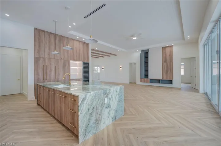 Kitchen featuring a large island with sink, light stone countertops, modern cabinets, pendant lighting, and parquet floors