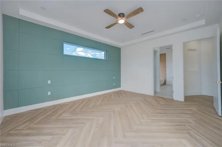 Spare room with a tray ceiling, ceiling fan, parquet floors, and an accent wall