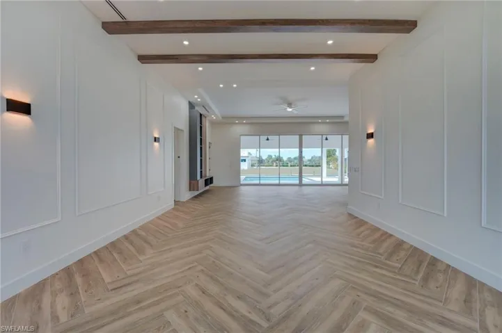 Unfurnished living room with a decorative wall, a ceiling fan, parquet flooring, beamed ceiling, and recessed lighting