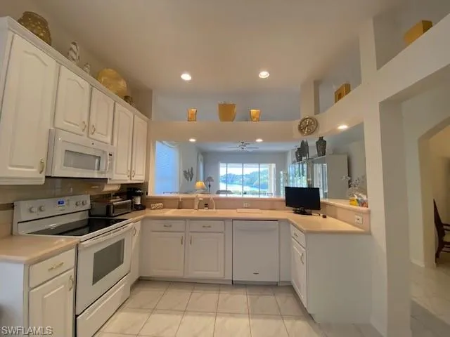 Kitchen with white appliances, white cabinetry, and kitchen peninsula