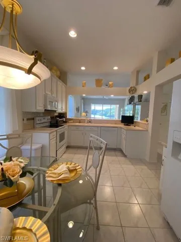 Kitchen with kitchen peninsula, white dishwasher, light tile patterned floors, range, and white cabinets
