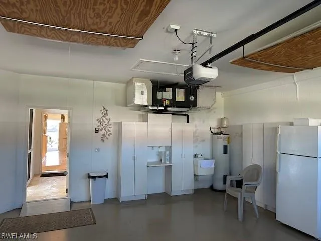 Garage with white refrigerator, electric water heater, sink, and a garage door opener