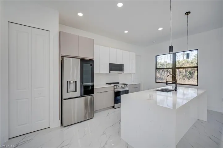 Kitchen with stainless steel appliances, decorative light fixtures, light marble finish floors, and light stone counters