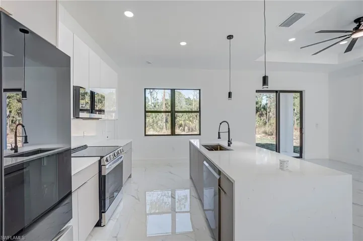 Modern kitchen featuring an expansive island with an undermount sink, stainless steel appliances, white cabinetry, and large format tile flooring