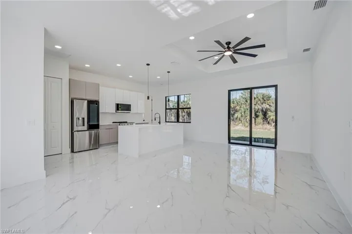 Kitchen with open floor plan, stainless steel appliances, an island with sink, light marble finish floors, and a ceiling fan
