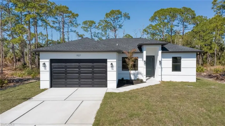 View of front of house featuring a front yard, roof with shingles, a garage, driveway, and stucco siding