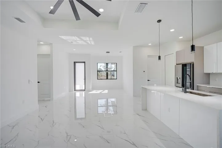 Kitchen featuring light marble finish floors, stainless steel fridge, white cabinets, pendant lighting, and light stone countertops
