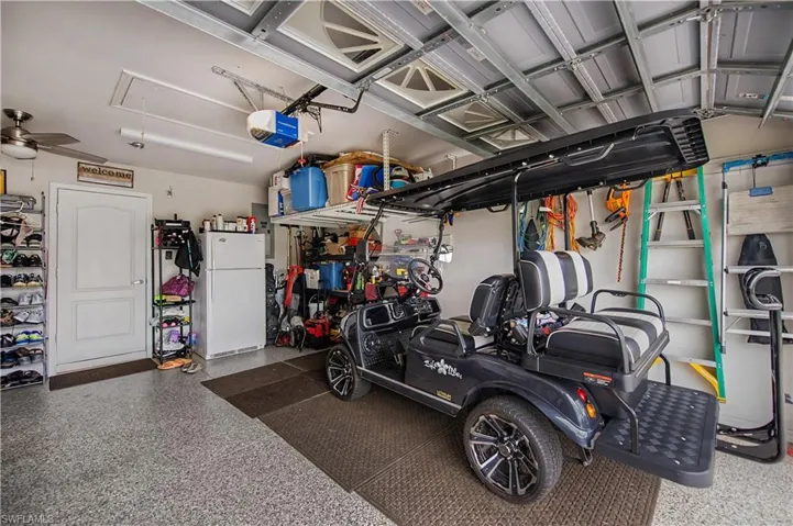 Spacious garage with speckled epoxy flooring, overhead storage racks, a white access door, a ceiling fan, and built-in shelving