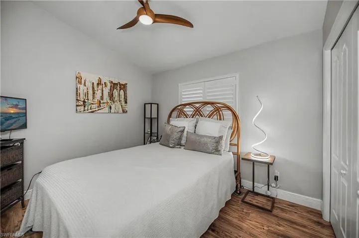 Room featuring wood-finish flooring, a ceiling fan with integrated lighting, a window with white louvered shutters, and a bifold closet door