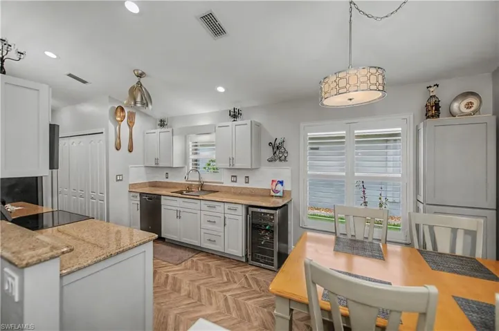 Kitchen featuring light cabinetry, granite countertops, stainless steel appliances, a built-in beverage cooler, and wood-finish flooring with a herringbone pattern