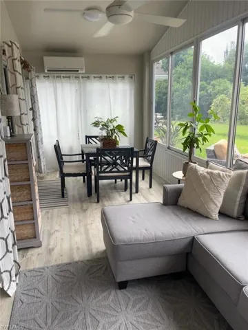 Light-filled sunroom featuring wood-finish flooring, a ceiling fan, abundant windows, and a wall-mounted air conditioning unit