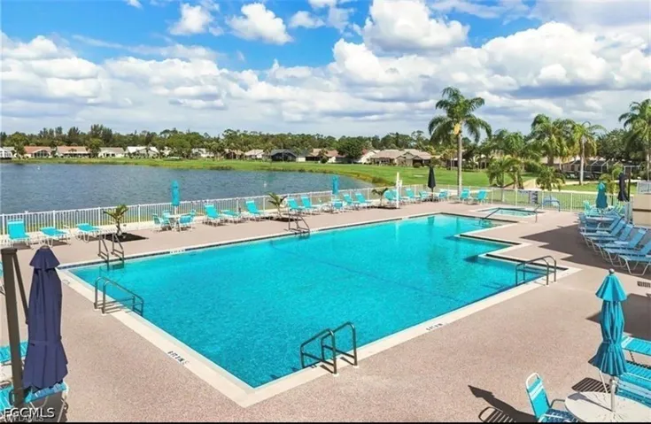 Community swimming pool with an integrated spa, expansive paver deck, and surrounding lake