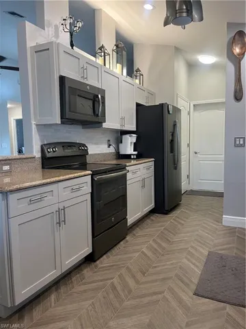 Modern kitchen featuring light gray cabinetry, stainless steel hardware, and speckled countertops