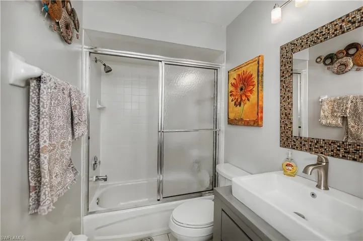 Bathroom featuring a white tub with sliding glass doors, a vessel sink with a brushed nickel faucet, a mosaic-tiled mirror, and track lighting