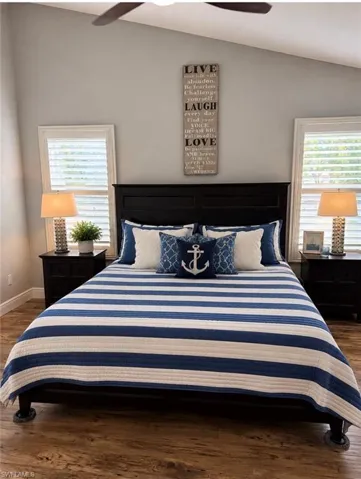Vaulted ceiling bedroom featuring wood-finish flooring, dual windows with plantation shutters, and a ceiling fan