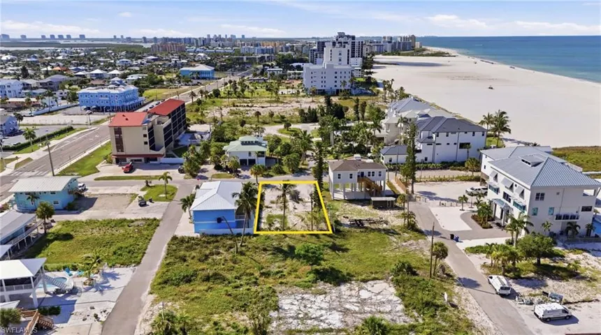 Cleared lot with existing palm trees, positioned between developed residential structures and a paved road