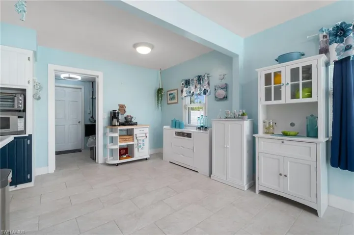 Kitchen with white cabinetry, white microwave, and light tile flooring