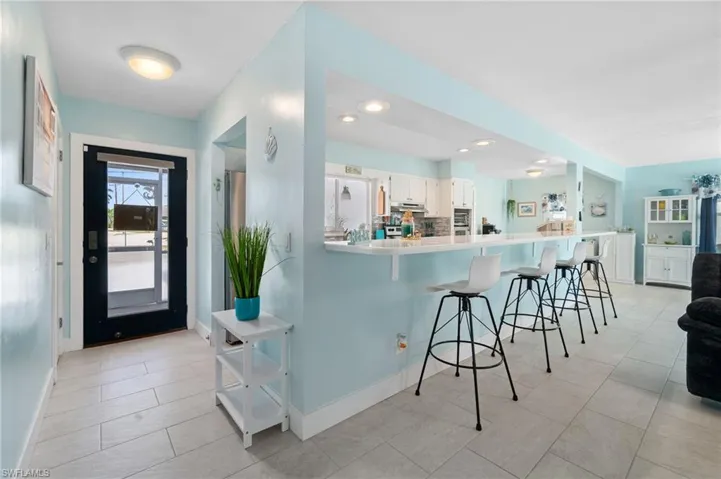 Kitchen featuring a kitchen breakfast bar, kitchen peninsula, white cabinets, and light tile floors