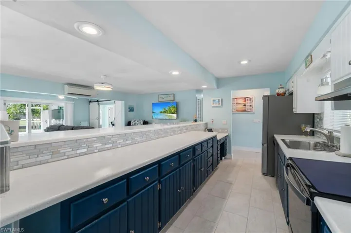 Kitchen featuring white cabinets, a wall mounted AC, sink, light tile floors, and blue cabinets