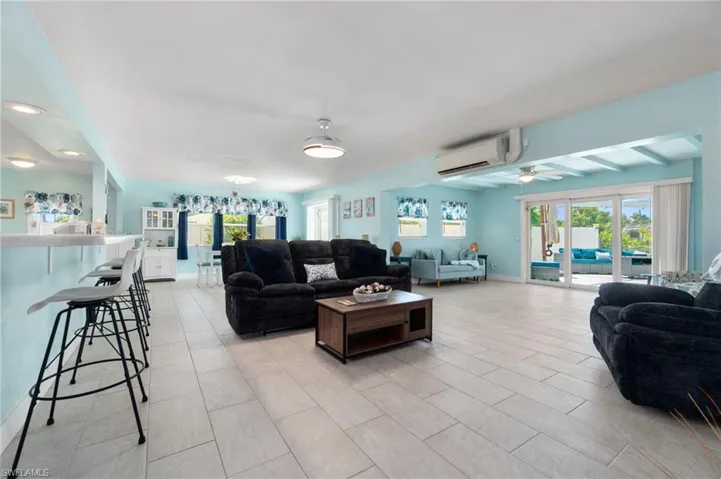 Living room featuring ceiling fan, beam ceiling, light tile flooring, and a wall mounted AC