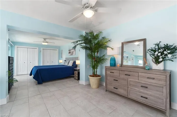 Bedroom featuring ceiling fan, light tile flooring, and multiple closets