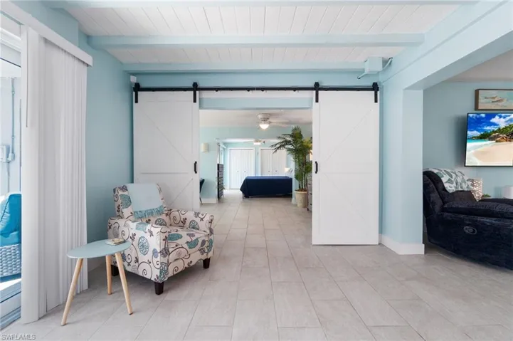 Living area with a barn door, beam ceiling, ceiling fan, and light tile floors