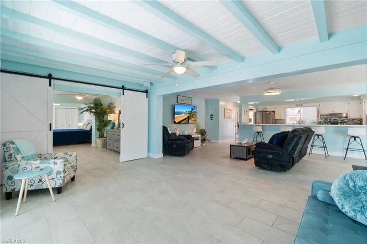 Living room with a barn door, beam ceiling, ceiling fan, and light tile floors