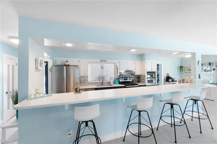 Kitchen featuring white cabinetry, stainless steel appliances, a breakfast bar area, backsplash, and light tile floors