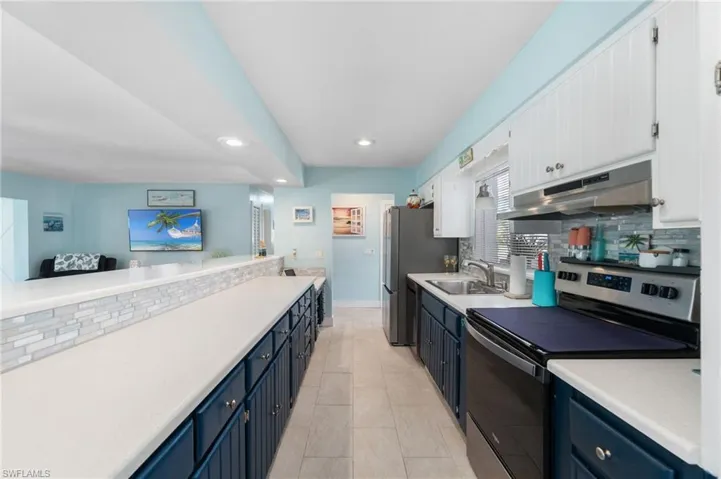 Kitchen with light tile flooring, blue cabinets, tasteful backsplash, electric range, and sink