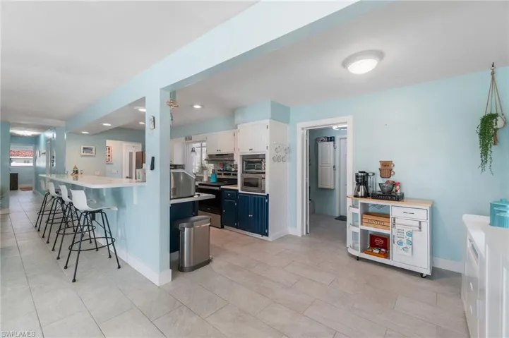 Kitchen with blue cabinetry, light tile floors, a breakfast bar, white cabinetry, and appliances with stainless steel finishes