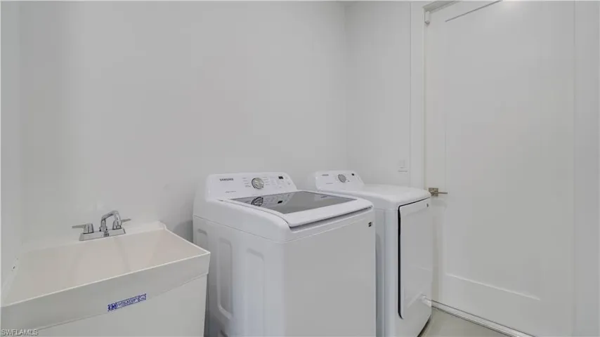 Indoor laundry room with Samsung large capacity washer & dryer, utility sink, & room for storage.