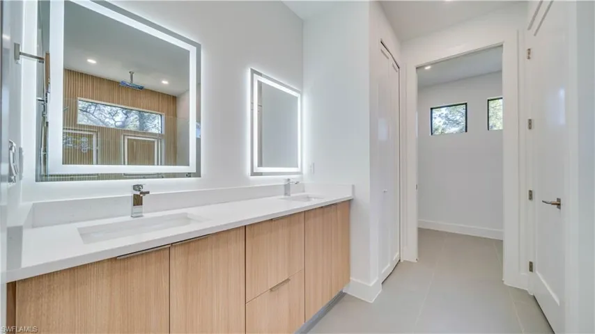 Primary bathroom with double sink vanity, custom cabinetry, backlit mirrors, quartz countertops, linen closet, and private water closet.