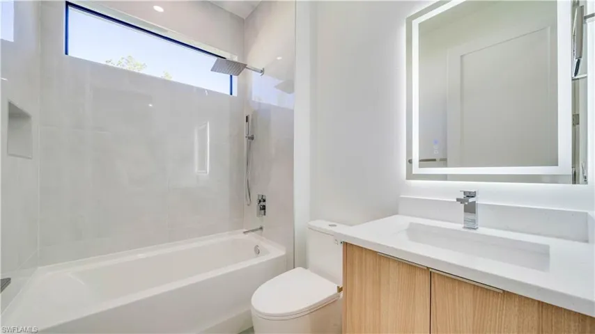 Guest bathroom with tub & shower combo, multiple shower heads, and a backlit mirror.
