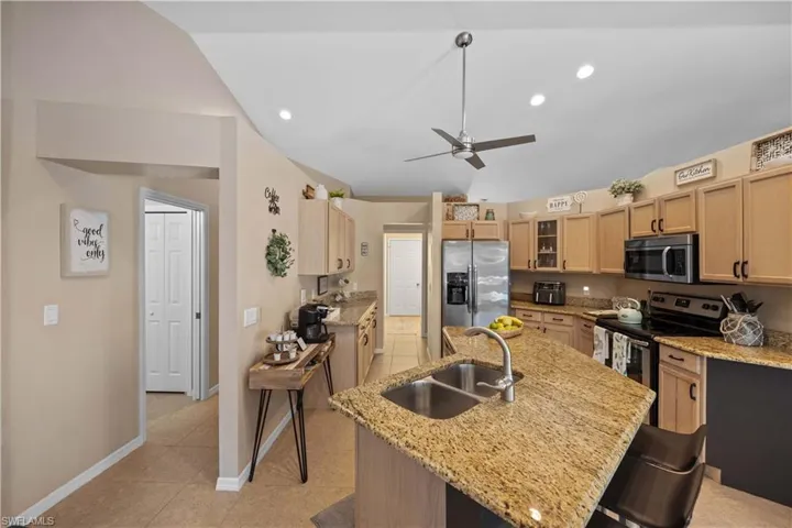 Kitchen with sink, light stone counters, light brown cabinets, an island with sink, and appliances with stainless steel finishes