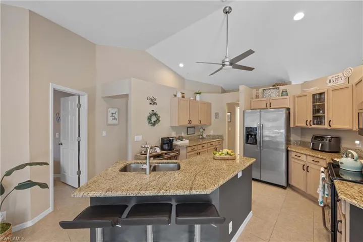 Kitchen with electric stove, stainless steel fridge with ice dispenser, a breakfast bar, a kitchen island, and sink